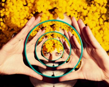 Image of a woman looking at the camera holding a magnifying glass. Purpose of image is to hone in on the woman's face because the post is about chronic illness and identity.